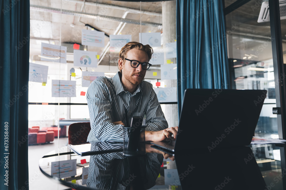 Poster caucasian man in optical spectacles using modern laptop computer for doing software developing durin