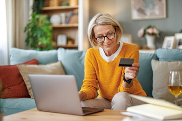 Mature  or senior woman using credit card for making online payment at home - 673365018