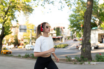 Confident sportswoman listening music through in-ear headphones while jogging in city