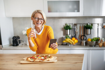Attractive mature woman eating delicious pizza in her kitchen