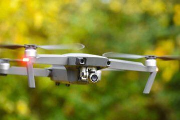 Drone with digital camera and fast rotating propellers flying taking video and pictures. Greenery...
