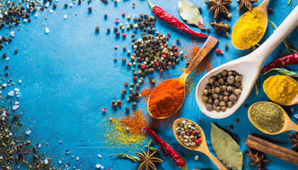 blue background a wooden spoon, pepper, cloves and other bright spices - obrazy, fototapety, plakaty