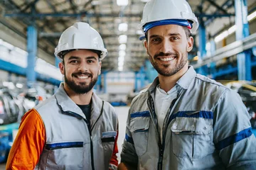 Foto op Plexiglas Zwei junge Männer Facharbeiter/Fachkräfte in Arbeitskleidung und Helmen lächelnd in einer Industriehalle © Tim B.