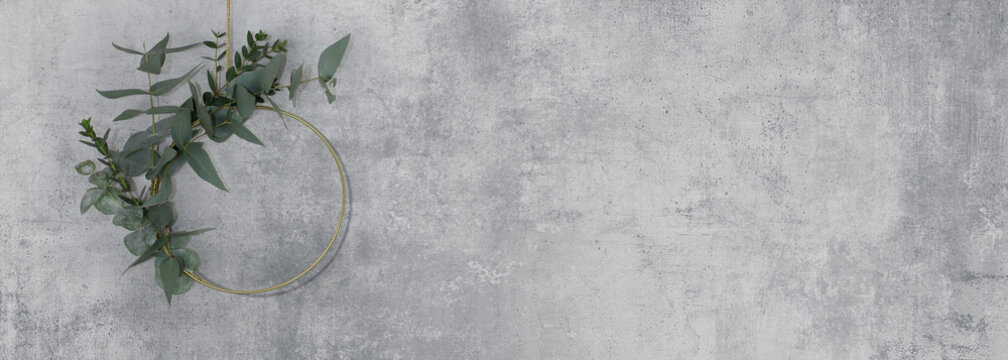 A metal ring decorated with leaves, hanging on a gold chain on a light concrete wall