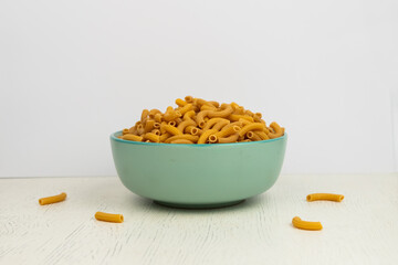 Fototapeta na wymiar pasta horns in a green bowl on a white background