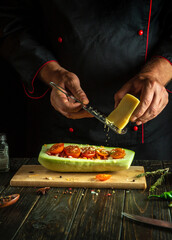 The cook adds cheese to the stuffed pumpkin on the kitchen table. The concept of cooking stuffed zucchini or an American national dish