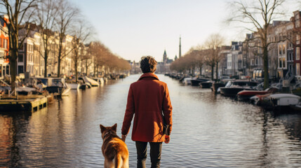 Man in an orange coat looking over a river in Amsterdam with his dog by his side on a sunny winter's day