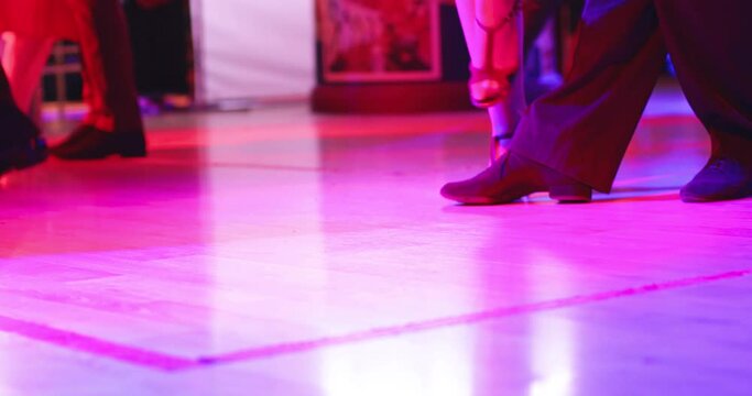 Dancing shoes of a couple, couples dancing traditional latin argentinian dance milonga in the ballroom, tango salsa bachata kizomba lesson, festival on wooden floor, purple, red and violet lights