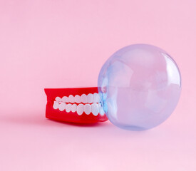 Artificial jaw and bubble of chewing gum on  pink background. Minimal art poster.