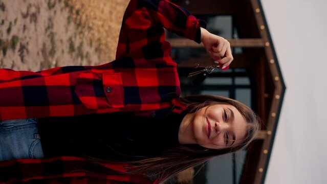 A girl holds a bunch of keys to her new home against the backdrop of wooden cottage in the woods in the countryside