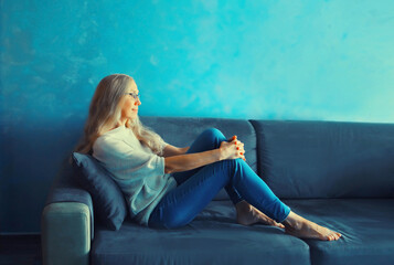 Relaxed caucasian middle-aged woman in eyeglasses resting in the room sitting on the couch at home