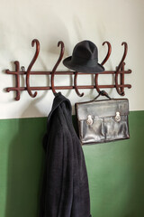 Black ancient leather briefcase, black hat and coat on the vintage wooden cloth hanger. The wall is...