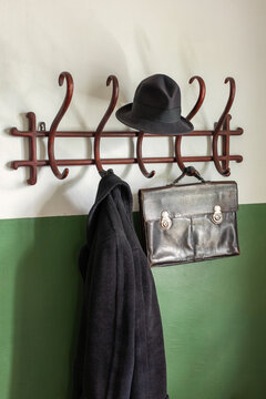 Black ancient leather briefcase, black hat and coat on the vintage wooden cloth hanger. The wall is half painted with green paint. Vertical photo