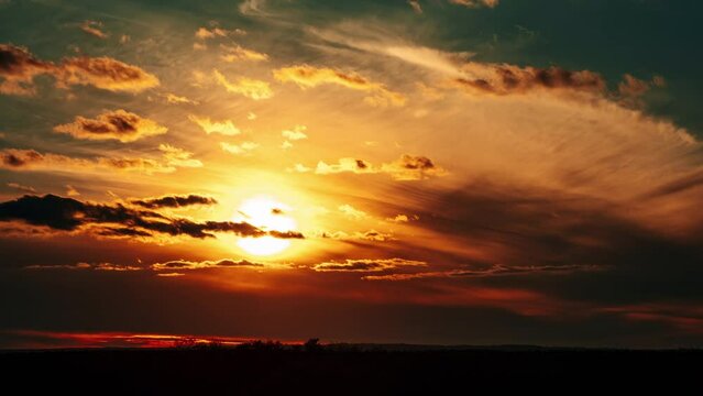 Amazing sunset in orange sky with dark dramatic clouds, Timelapse. 4K. Bright sun setting down above the horizon. Colorful sunset, epic clouds. Vibrant color. Time-lapse. Sundown, cloudscape