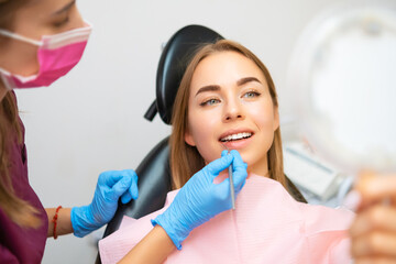 Woman Looking To Mirror After Teeth Treatment In Modern Clinic.