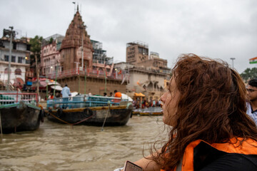 Fototapeta na wymiar Woman looks the view of the river Ganges with its boats, people and sacred water of Varanasi in India