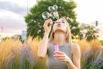 A smiling lady with long hair blows soap bubbles, spreading happiness in the park during the...