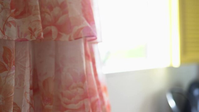 Pink dress with flowery pattern hanging nearby window before wedding in New Zealand