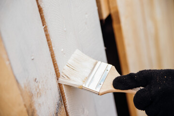 A gloved hand paints a wooden background and boards.Painting works indoors and outdoors. Renovation...
