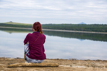 Girl sitting on the beach near the shore of lake Tambukan and contemplating a beautiful mountainous view in front of her.