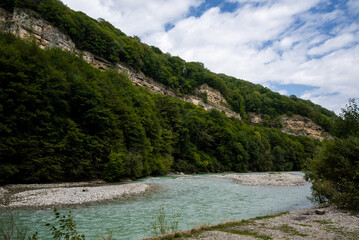 Mountain river in the mountains, green forest nearby, blue sky