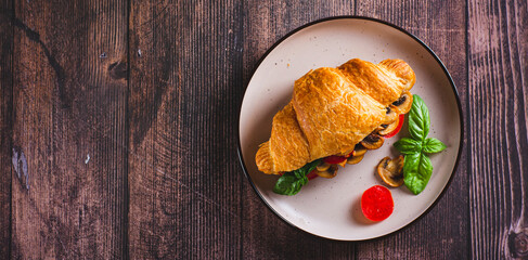Fresh croissant with fried mushrooms, tomatoes and basil on a plate top view web banner