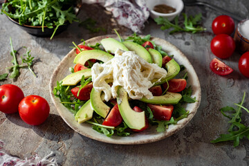 A dish for the whole family for lunch: a spicy salad with avocado, cheese, arugula, cherry tomatoes, spices and olive oil. Diet salad for breakfast. View from above.