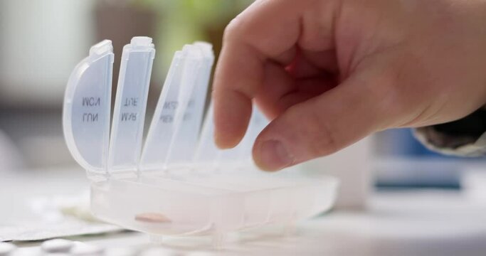 Male hand putting pills into open pill organizer or plastic pillbox
