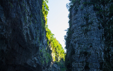 A rocky gorge in Abkhazia with steep walls and a narrow road between them on a sunny summer day