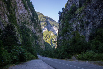 A rocky gorge in Abkhazia with steep walls and a narrow road between them on a sunny summer day