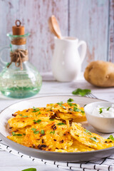 Potato latkes with herbs and sour cream on a plate on the table vertical view