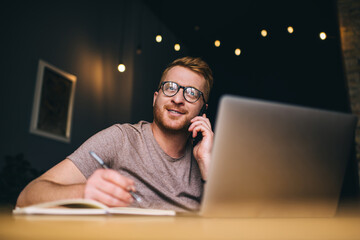 Skilled Caucasian journalist with modern laptop and textbook planner making mobile communication in...