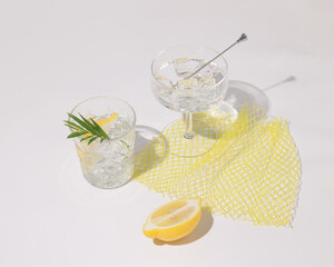 Summer refreshing drink or alcoholic cocktail with ice and lemon slices on white background, mesh...