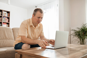 Successful happy freelancer working on laptop at home. A man sits on the sofa and uses a laptop to shop and communicate online