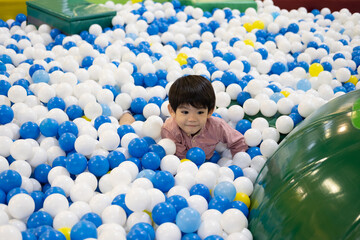 A little Asian boy was playing hide-and-seek among the balls.