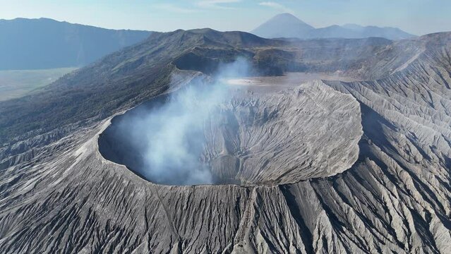 Aerial 4K footage of the Bromo volcano crater caldera with smoke coming. An active volcano in Tengger Semeru National Park in East Java, Indonesia.