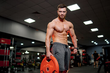Fototapeta na wymiar A shirtless man holding a red disc in a gym. A Fit Athlete Demonstrating Strength and Balance with a Vibrant Gym Prop