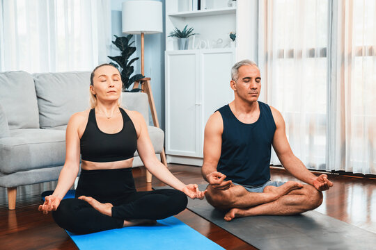 Happy Active Senior Couple In Sportswear Being Doing Yoga In Meditation Posture On Exercising Mat At Home. Healthy Senior Pensioner Lifestyle With Peaceful Mind And Serenity. Clout