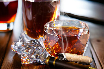 A glass of Scotch whiskey with ice and a cigar stands on the window close-up.