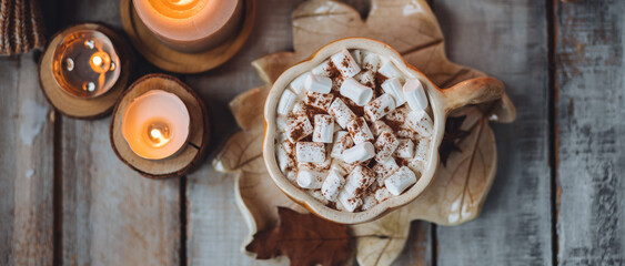Flat lay top view. Spicy sweet fall hot drink: delicious pumpkin latte with cinnamon, marshmallow. Served in handmade artisan mug in shape of pumpkins, cozy home decor with candles, dry leaves banner