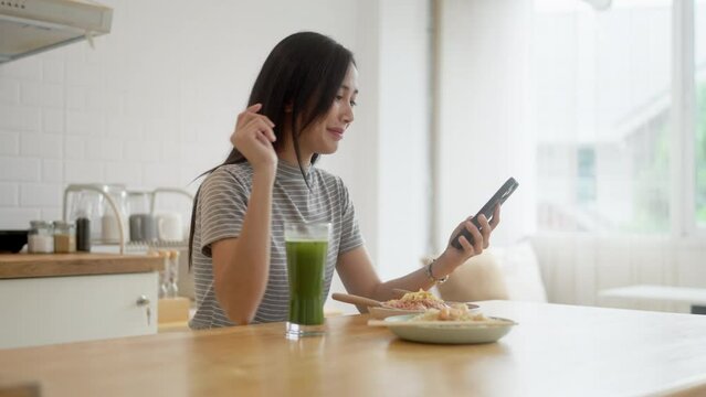 Asian woman watching her smartphone while eating food.