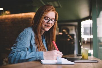 Cheerful woman taking notes in notebook in cafe