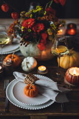 Elegant seasonal fall table setting with floral composition in a pumpkin vase as a centrepiece. White wine, burning candles, romantic cozy atmosphere of family dinner, private autumn wedding