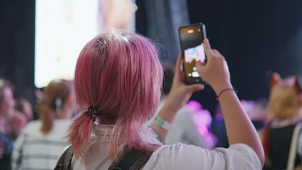 Girl takes video on phone at music anime cosplay gaming convention concert.