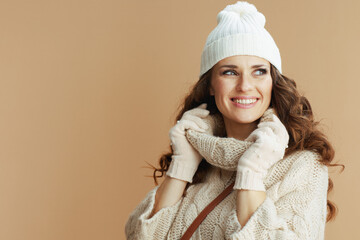 happy stylish woman in beige sweater, mittens and hat on beige