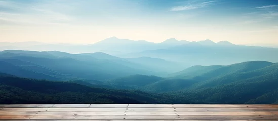 Deurstickers In the misty morning landscape you can admire a wooden table against the backdrop of a blurred mountain view The cool sensation in blue hues adds to the overall ambiance © 2rogan