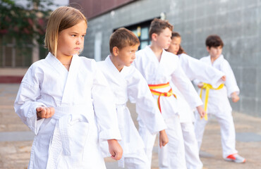 Fototapeta na wymiar Confident tween girls and boys in white kimonos practicing new techniques during outdoors group taekwondo class on summer day