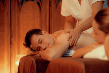 Obraz na płótnie Canvas Caucasian couple customer enjoying relaxing anti-stress spa massage and pampering with beauty skin recreation leisure in warm candle lighting ambient salon spa at luxury resort or hotel. Quiescent