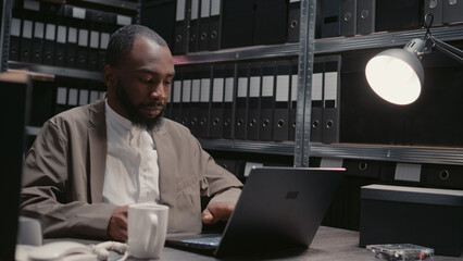 Male inspector analyzing physical evidence in archive, looking at case files research with criminal...