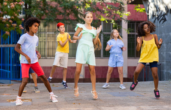 Group of multiracial positive kids jumping while performing street dance outdoors.